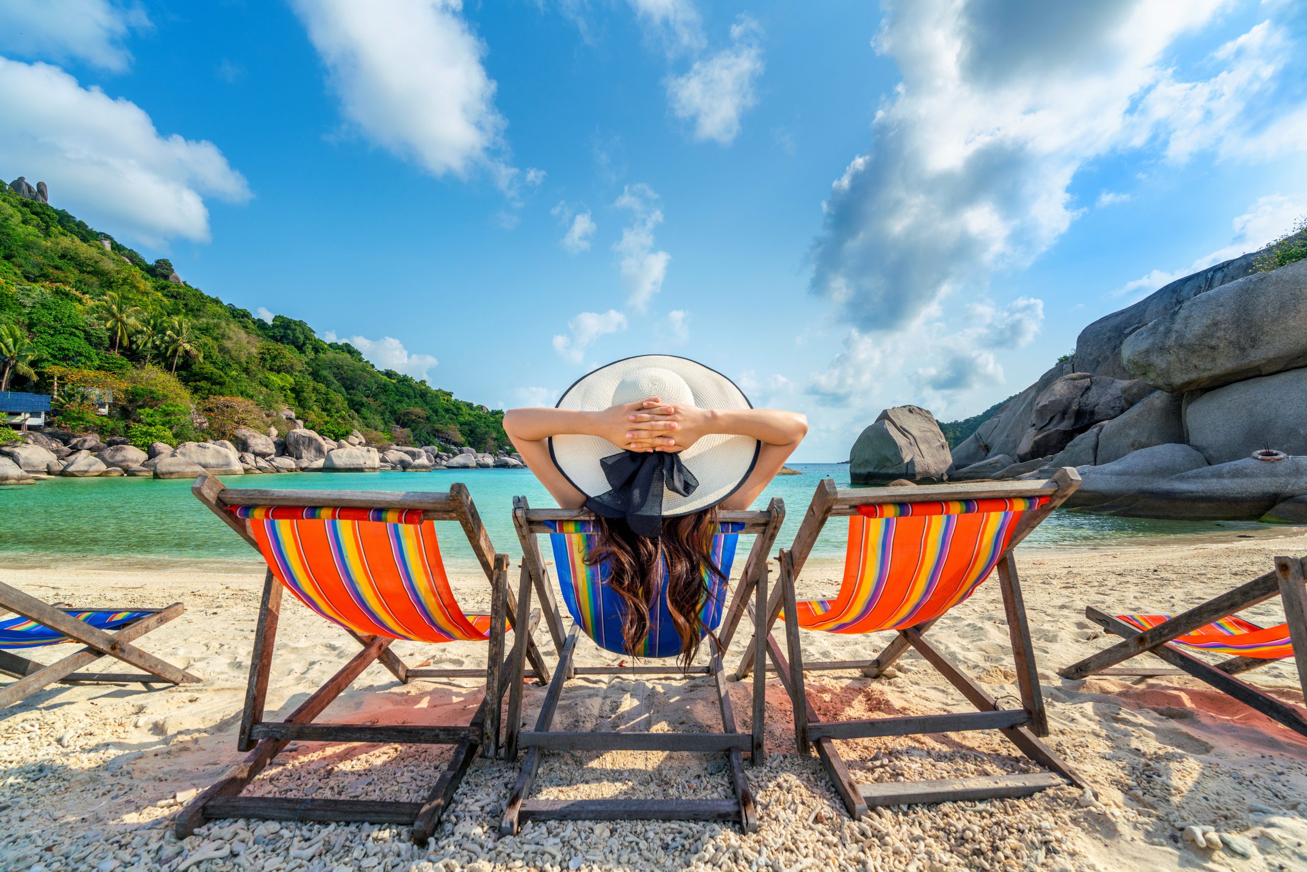 Woman with hat sitting on chairs beach in beautiful tropical bea
