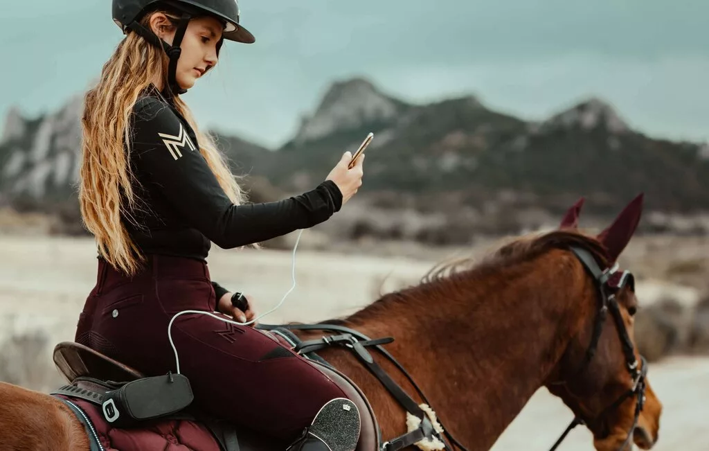 Frau auf einem Pferd mit Smartphone in der Hand