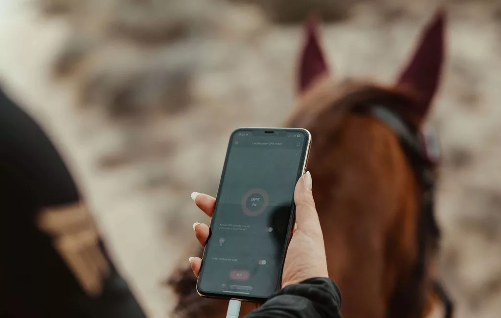 Smartphone in der Hand auf einem Pferd mit Mobile GPS Tracker App von PAJ