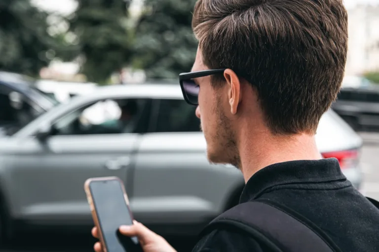 A young man in sunglasses uses a smartphone, close-up